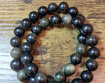 Könnte beinhalten: Ein schwarzes und grünes Perlenarmband mit glänzender Oberfläche. Das Armband besteht aus runden Perlen und ist übereinander gelegt.