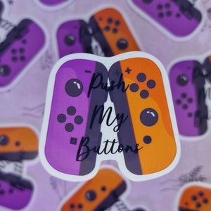 May include: A sticker showing two game controllers, one purple and one orange, with the words "Push My Buttons" in white. The controllers are set against a light purple background with other controller stickers.