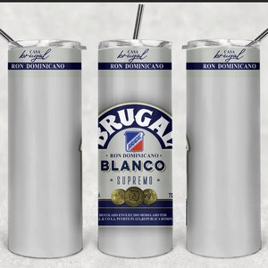 May include: A set of three stainless steel tumblers with lids and straws. The tumblers feature a white background with the "Casa Brugal" and "Ron Dominicano" logos. The center tumbler displays the "Brugal Blanco Supremo" logo.