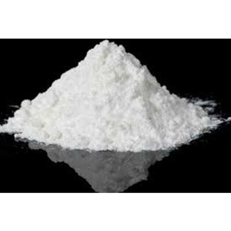 May include: A large pile of white powder on a black surface. The powder is finely ground and has a smooth texture.