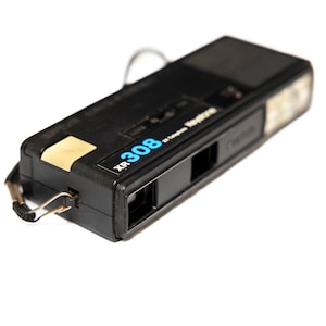 May include: A black and silver 35mm film camera with a built-in flash. The camera has a strap and the text "XR 308 35 Camera" is printed on the side.