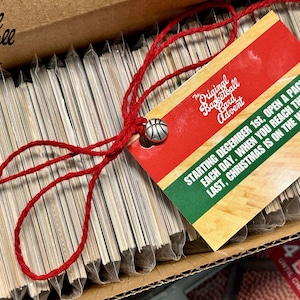 May include: A stack of sealed envelopes tied with red string and a tag that reads "The Original Basketball Card Advent. Starting December 1st, open a pack each day. When you reach the last, Christmas is on the way!"