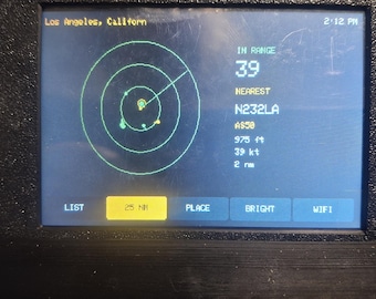 May include: A black electronic device with a rectangular screen displaying a radar interface. The screen shows Los Angeles, California, 2:12 PM, IN RANGE 39, NEAREST N232LA, A550, 975 ft, 39 kt, 2 nm, and buttons labeled LIST, 25 NM, PLACE, BRIGHT, WIFI.