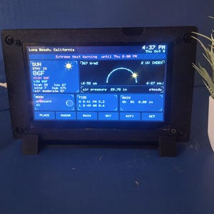May include: A black rectangular digital weather station display featuring a blue screen with white text and icons. The screen shows Long Beach, California, current time, date, temperature, solar radiation, UV index, moon phase, tide, and rain data.