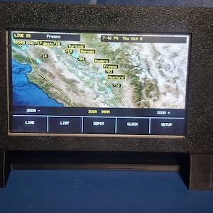 May include: A black rectangular digital display monitor with a textured frame, showing a live map interface of California with city labels like Fresno, Turlock, and Hanford. The screen includes navigation buttons labeled LINE, LIST, DEPOT, CLOCK, and SETUP.