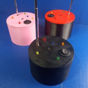 May include: Three 3D printed cylindrical bases with a variety of colored LED lights and a toggle switch on each. The bases are pink, black, and red.