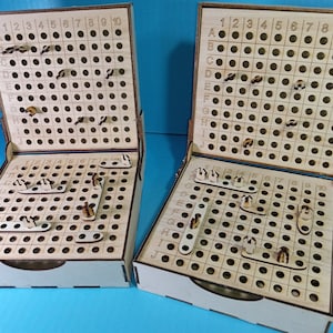 Può includere: Due tavoli da gioco in legno con una griglia di fori e piccoli pezzi di legno. I tavoli sono aperti e mostrano la griglia e i pezzi. I tavoli sono etichettati con le lettere A a J e i numeri da 1 a 10.