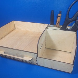 May include: A wooden desk organizer with a drawer, two compartments for pens and a compartment for scissors. The organizer is made of light wood and has a natural finish.