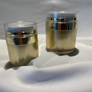 May include: Two gold and clear plastic pump bottles with white lids. The bottles are on a white surface.