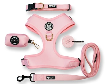 May include: A pink dog harness, leash, collar, and poop bag holder set with black hardware and the text "Belle Ella Pup Co."
