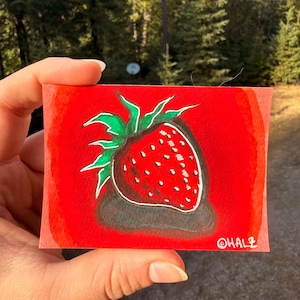 Puede incluir: Pequeña pintura rectangular de una fresa. La fresa es roja con semillas blancas y hojas verdes. El fondo es un degradado de rojo. La firma del artista, "OHALZ", está en la esquina inferior derecha.