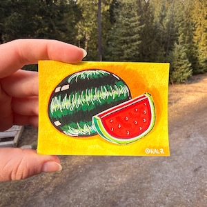 Puede incluir: Pequeña pintura cuadrada de una sandía sobre fondo amarillo. La sandía es de rayas verdes y negras, con interior rojo y semillas negras. La pintura está firmada "@HALZ".
