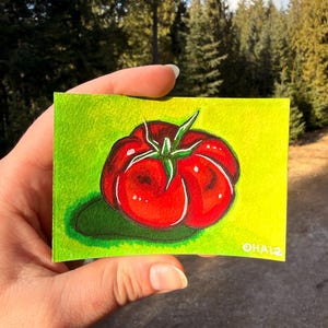 Puede incluir: Pequeña pintura rectangular de un tomate rojo con hojas verdes y una sombra verde. El tomate está sobre un fondo verde-amarillo brillante. La firma del artista, "OHALZ", está en la esquina inferior derecha.