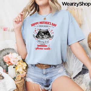 Può includere: T-shirt azzurra con la scritta "Happy Mother's Day From Inside" e un'immagine ecografica. La maglietta presenta anche la scritta "Mommy to be loading... please wait" in rosso.