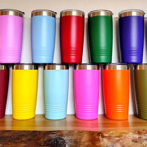 May include: A set of three ceramic mugs with a speckled, matte finish. The mugs are in shades of cream, light brown, and dark brown. Each mug has a simple, minimalist design and a rounded handle.