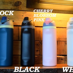 May include: Four insulated water bottles in peacock blue, black, cherry blossom pink, and white. Each bottle has a matching colored lid with a contrasting accent color. The text "PEACOCK BLUE", "BLACK", "CHERRY BLOSSOM PINK", and "WHITE" are displayed.