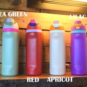 May include: Four colorful water bottles in pea green, red, apricot, and lilac. Each bottle has a contrasting colored lid and a matching colored band. The bottles are displayed on a wooden surface with the colors labeled.
