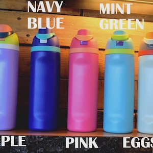 May include: Five colorful water bottles in purple, navy blue, pink, mint green, and eggshell. Each bottle has a contrasting colored lid and the names of the colors are written above the bottles. The bottles are displayed on a wooden surface.