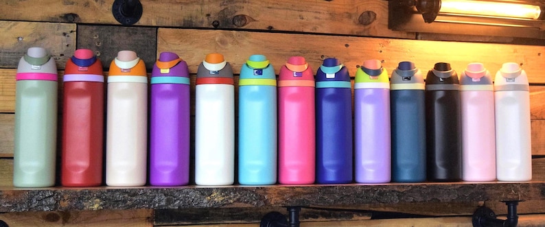 May include: A collection of colorful insulated water bottles displayed on a wooden shelf. The bottles come in various colors, including pink, red, blue, and white, with matching lids. Each bottle is approximately 10 inches tall.
