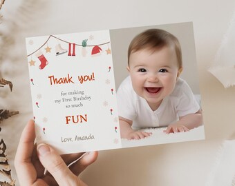 May include: A white thank you card with red and white snowflakes and a red and white string of Christmas ornaments. The card says "Thank you! for making my First Birthday so much FUN Love, Amanda". A photo of a baby is on the right side of the card.