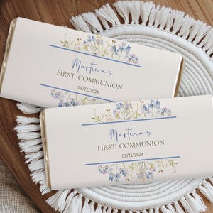 Puede incluir: Dos envoltorios de barra de chocolate blanco con diseños florales azules y verdes. El texto en los envoltorios dice "Martina's First Communion 09/21/2024".