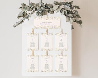 May include: A white board displays table assignments for Catherine's First Communion. The cards are decorated with floral accents and held by wooden clips. The top card reads "Please Find Your Seat".