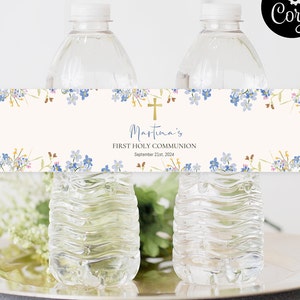 Puede incluir: Etiquetas para botellas de agua con diseño floral. Las etiquetas presentan flores de acuarela azules y amarillas, una cruz dorada y el texto "Martina's First Holy Communion September 21st, 2024". Las etiquetas están envueltas alrededor de botellas de agua transparentes.