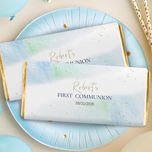 Puede incluir: Dos envoltorios de barra de chocolate de acuarela azul y blanca con detalles dorados. El envoltorio superior dice "Robert's Communion". El envoltorio inferior dice "Robert's First Communion 09/21/2025".