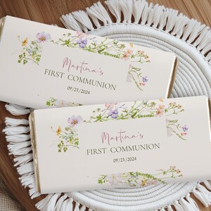 Puede incluir: Dos envoltorios de barra de chocolate blanco con diseños florales y el texto "Martina's First Communion 09/21/2024".
