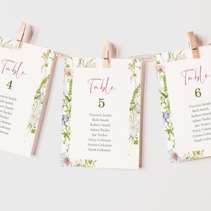May include: Three white table cards with floral borders and pink calligraphy. The cards are numbered 4, 5, and 6 and list names for each table.