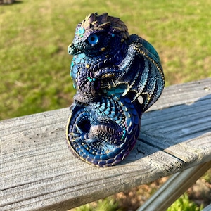 Peut inclure: Une tasse en céramique blanche avec une anse noire et le texte "But First, Coffee" en noir, en gras. La tasse est posée sur une surface blanche.