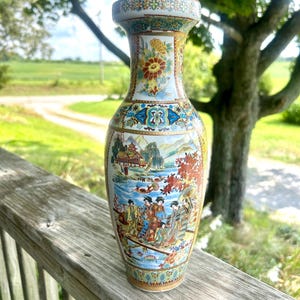 May include: A ceramic vase featuring a narrow neck and a bulbous body decorated with intricate, colorful illustrations of figures in traditional attire, a landscape with a pagoda, and floral patterns in shades of red, blue, gold, and green.