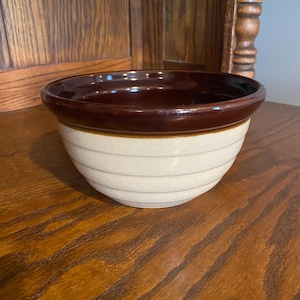 May include: A brown and cream ceramic bowl with a brown rim. The bowl has a white glaze with brown stripes.