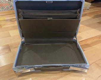 May include: Open, light blue briefcase with a silver clasp and handle. The interior features brown compartments and a large open space. The briefcase is designed for carrying documents and other business essentials.