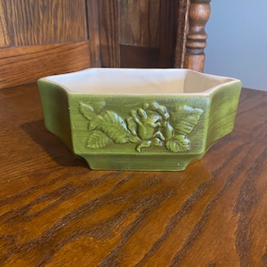 May include: A green hexagonal ceramic planter with a raised floral design. The planter has a white interior and is ideal for displaying small plants or flowers.