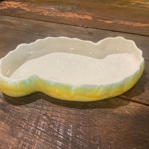 May include: A yellow and white ceramic planter shaped like a leaf. The planter has a crackled glaze and a scalloped edge.