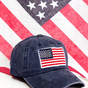May include: A dark blue baseball cap with a red, white, and blue American flag embroidered on the front.