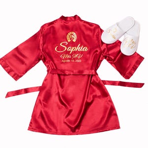 A red satin robe with gold text and a gold horseshoe on the back, along with a pair of white slippers.