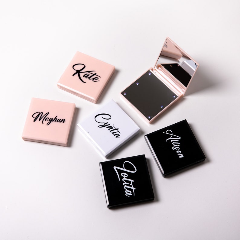 May include: Five compact mirrors with personalized names: Kate, Meghan, Cynthia, Allison, and Jolita. The mirrors are in pink, white, and black.
