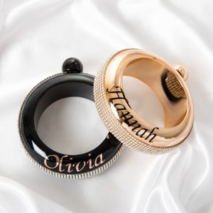 May include: Two personalized black and gold bangle bracelets with rhinestones. The black bracelet has the name "Olivia" engraved on it and the gold bracelet has the name "Hannah" engraved on it.