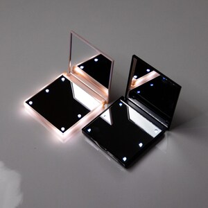 May include: Two compact mirrors with built-in LED lights. One mirror is black and the other is pink.