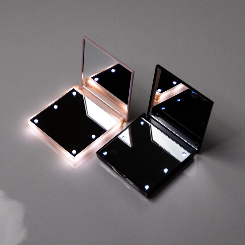 May include: Two compact mirrors with built-in LED lights. One mirror is black and the other is pink.
