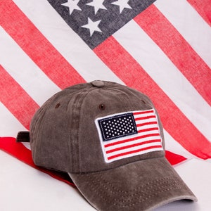 May include: A brown baseball cap with a small American flag patch on the front. The cap has a curved brim and a mesh back.