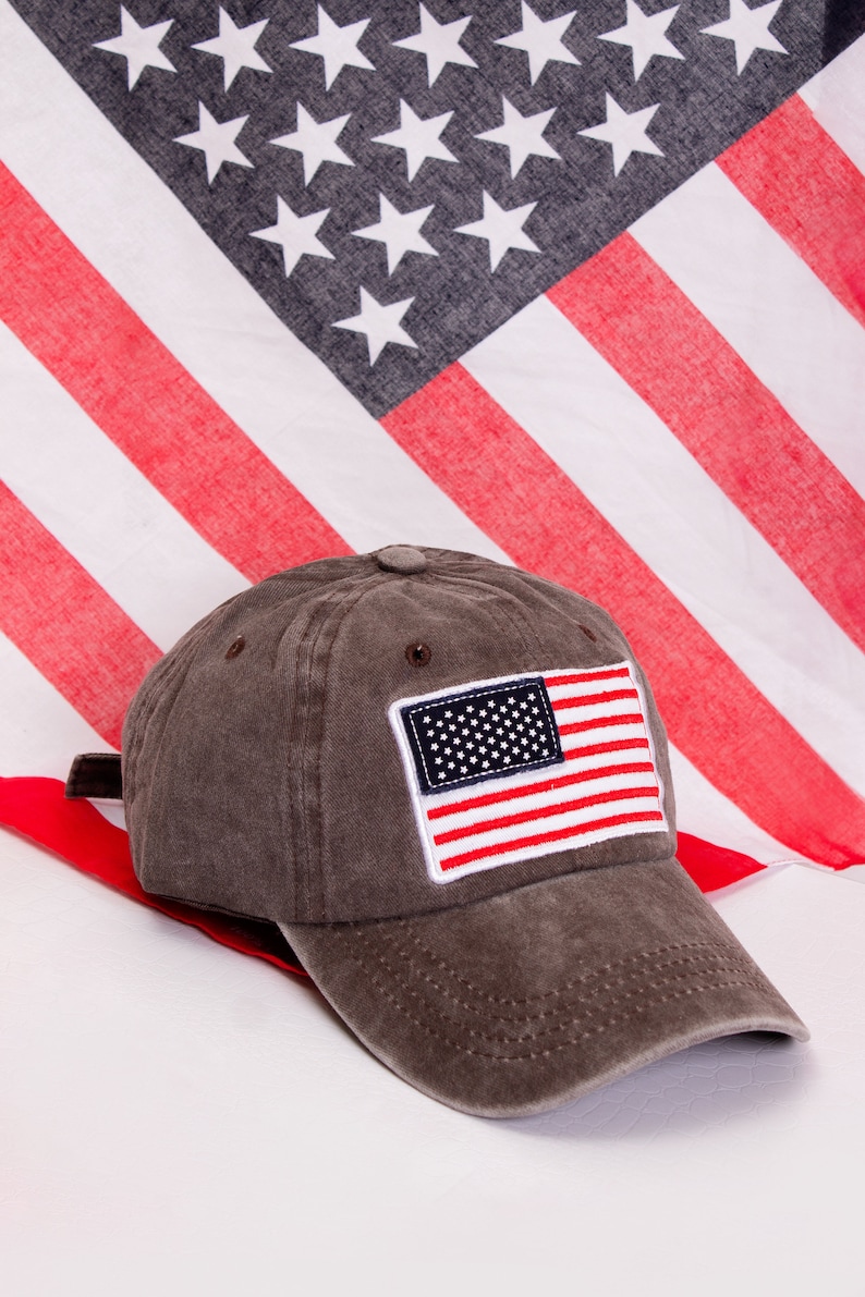 May include: A brown baseball cap with a small American flag patch on the front. The cap has a curved brim and a mesh back.