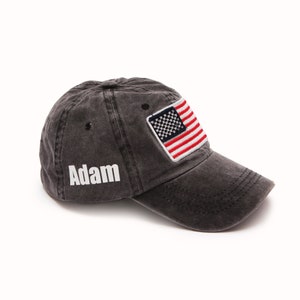 May include: A black, distressed, cotton baseball cap with a white embroidered name "Adam" on the front and a red, white, and blue American flag patch on the side.