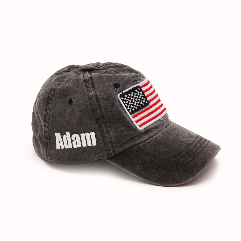 May include: A black, distressed, cotton baseball cap with a white embroidered name "Adam" on the front and a red, white, and blue American flag patch on the side.
