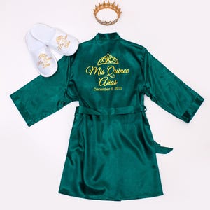 a green satin robe with gold text and a crown, along with white slippers and a gold crown.