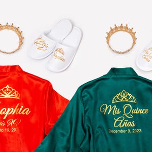 a collection of items related to a special occasion, including two robes, two crowns, and two pairs of slippers. The robes are red and green, and each one has a name and date printed on them. The crowns are gold and have a tiara design. The slippers are white and have a tiara design as well.
