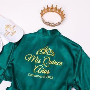 a green satin robe with gold text and a crown, along with white slippers and a gold crown.