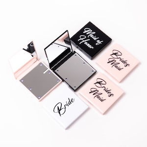May include: Four compact mirrors with LED lights. The mirrors are white, black, and pink. The mirrors have the words "Bride", "Maid of Honor", and "Bridesmaid" written on them.